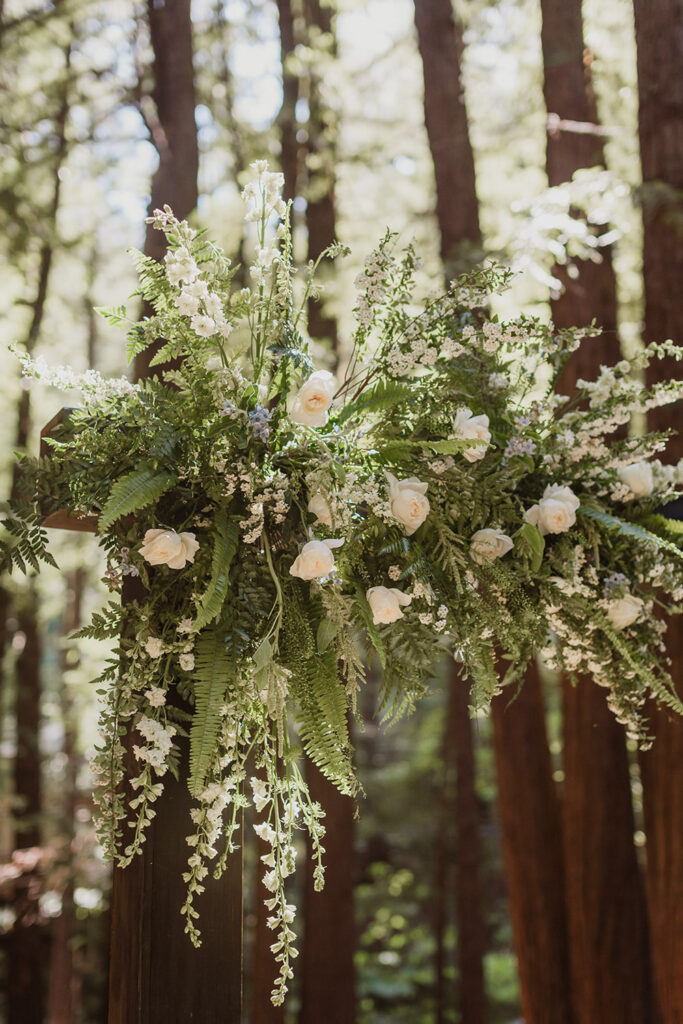white and green floral arrangement on ceremony arbor in the forest